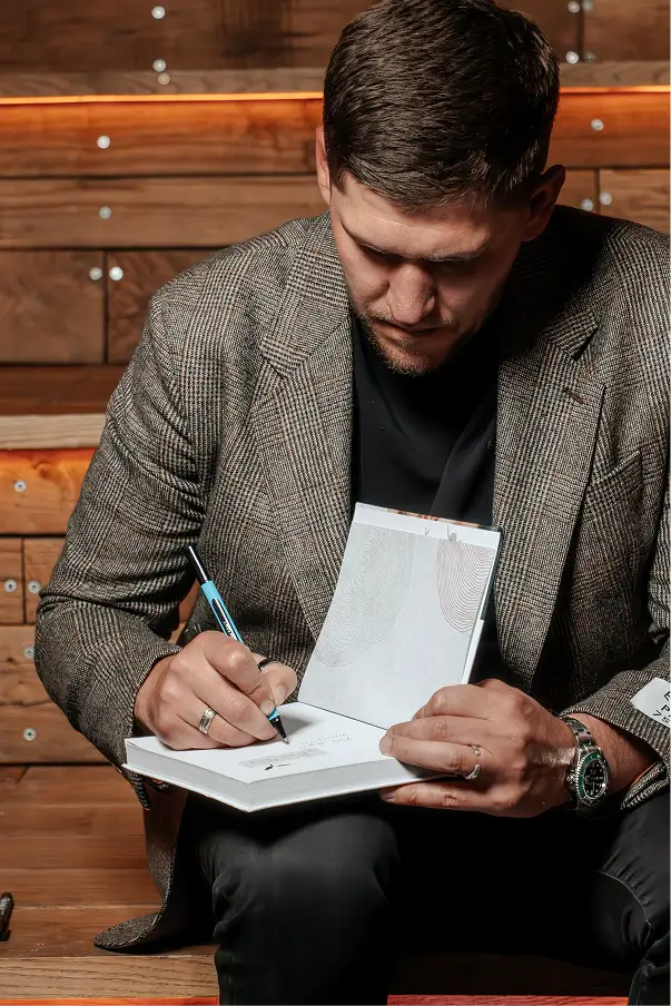 Ihor Fostenko in a suit sitting and writing in a notebook with a pen.

